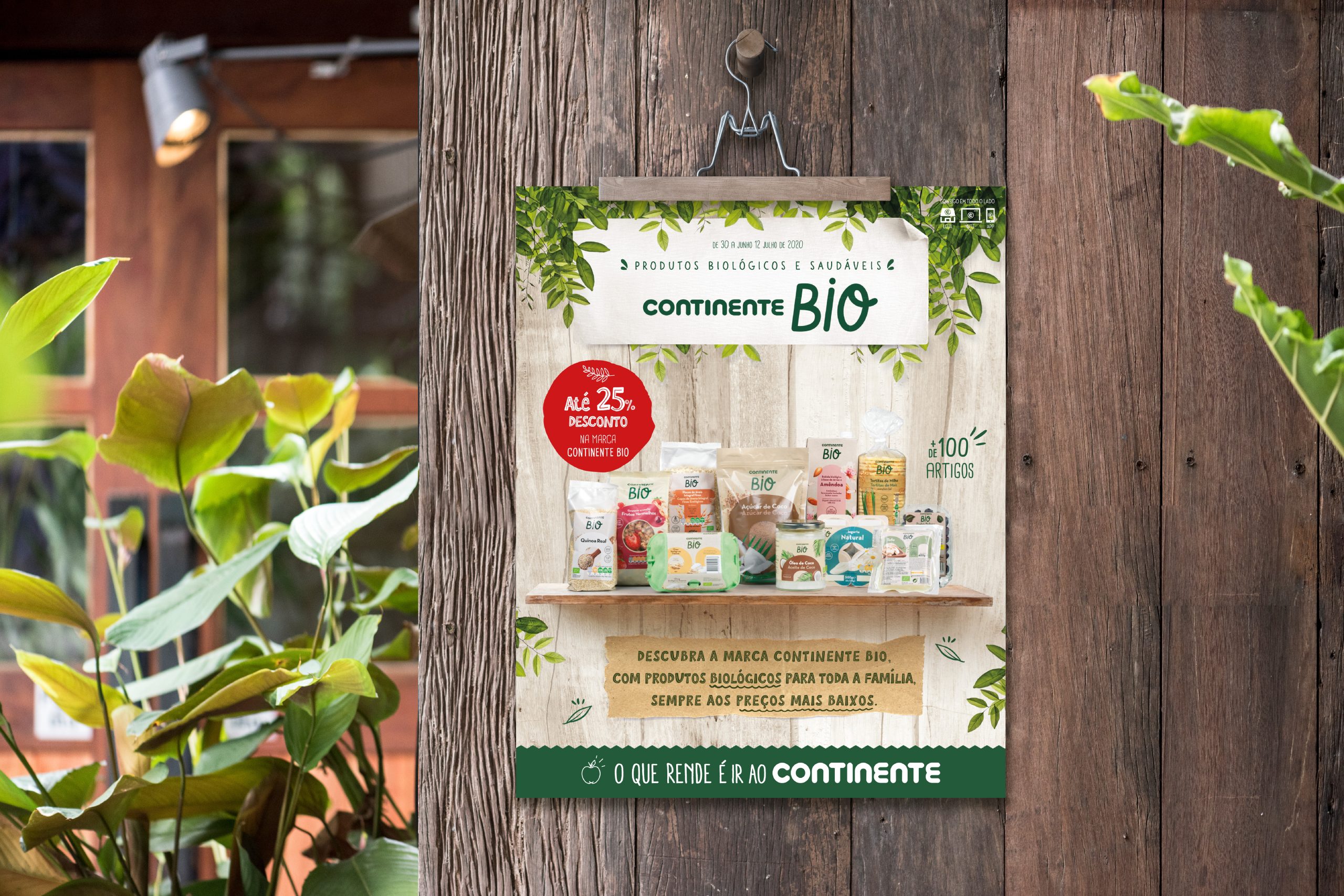 Continente Bio cover campaign poster hanging on a wooden background, surrounded by plants and natural elements, showcasing organic products with discounts.